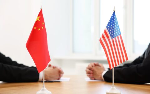 Diplomats,Negotiating,During,Meeting,At,Table,Indoors,,Focus,On,Flags