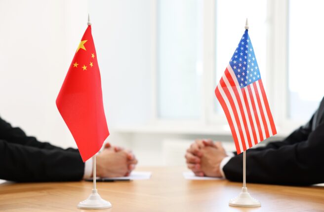 Diplomats,Negotiating,During,Meeting,At,Table,Indoors,,Focus,On,Flags