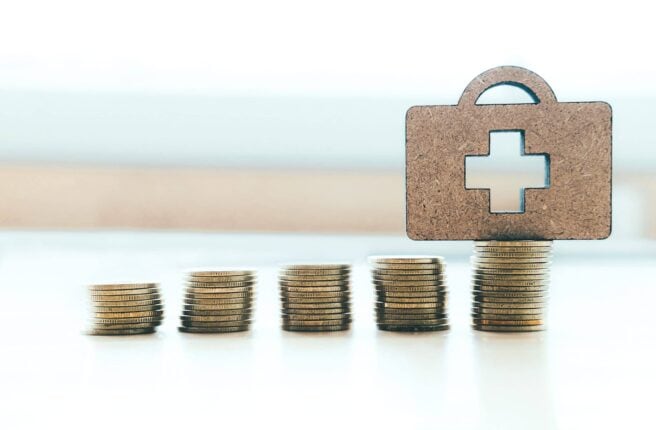 Health insurance copyspace background idea concept. Coin stacks and medical bag wood.