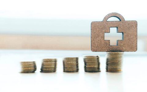 Health insurance copyspace background idea concept. Coin stacks and medical bag wood.