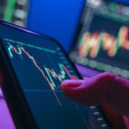 Close,Up,Of,Trader,Hand,Holding,Smartphone,,Using,Trading,Application