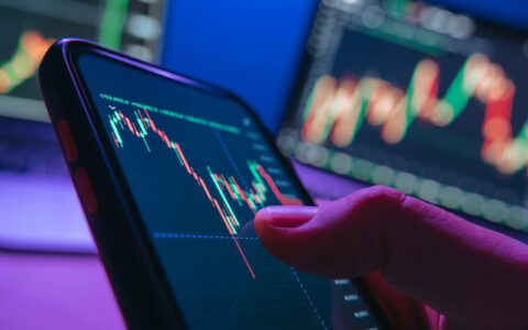 Close,Up,Of,Trader,Hand,Holding,Smartphone,,Using,Trading,Application