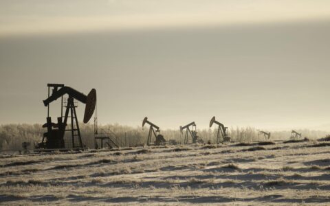 A field with oil pump jacks surrounded by greenery under a cloudy sky and sunlight
